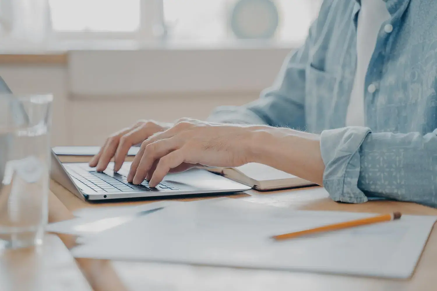 Cropped shot of man using laptop computer at home, male hands typing on keyboard on kitchen table. Closeup of technology in use and work remotely online concept